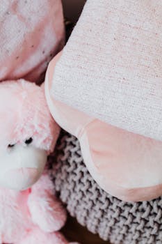 一只粉红色的泰迪熊特写镜头，依偎在色彩柔和的纹理枕头之间