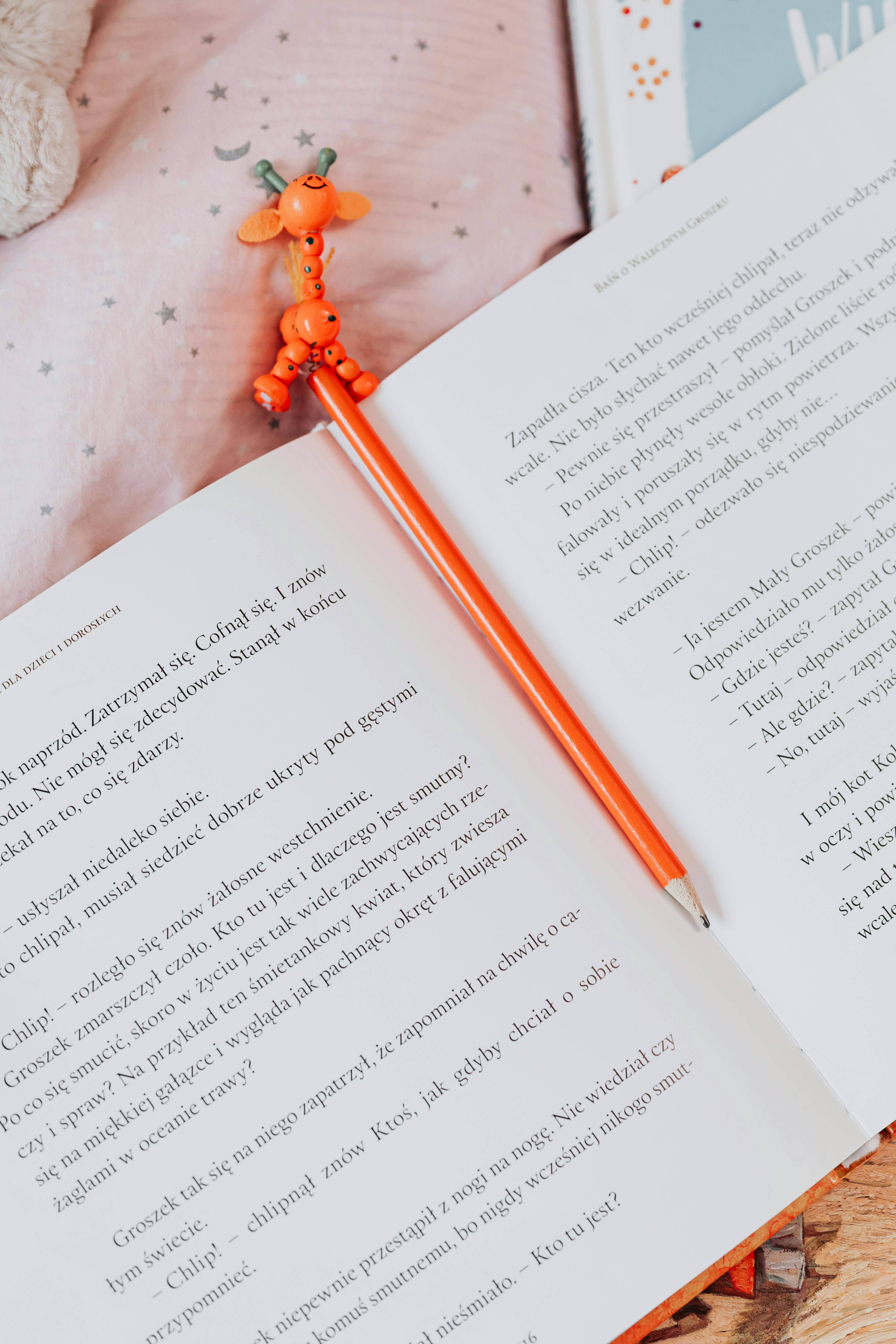 An open book with an orange pencil featuring a giraffe topper, perfect for education and creativity.