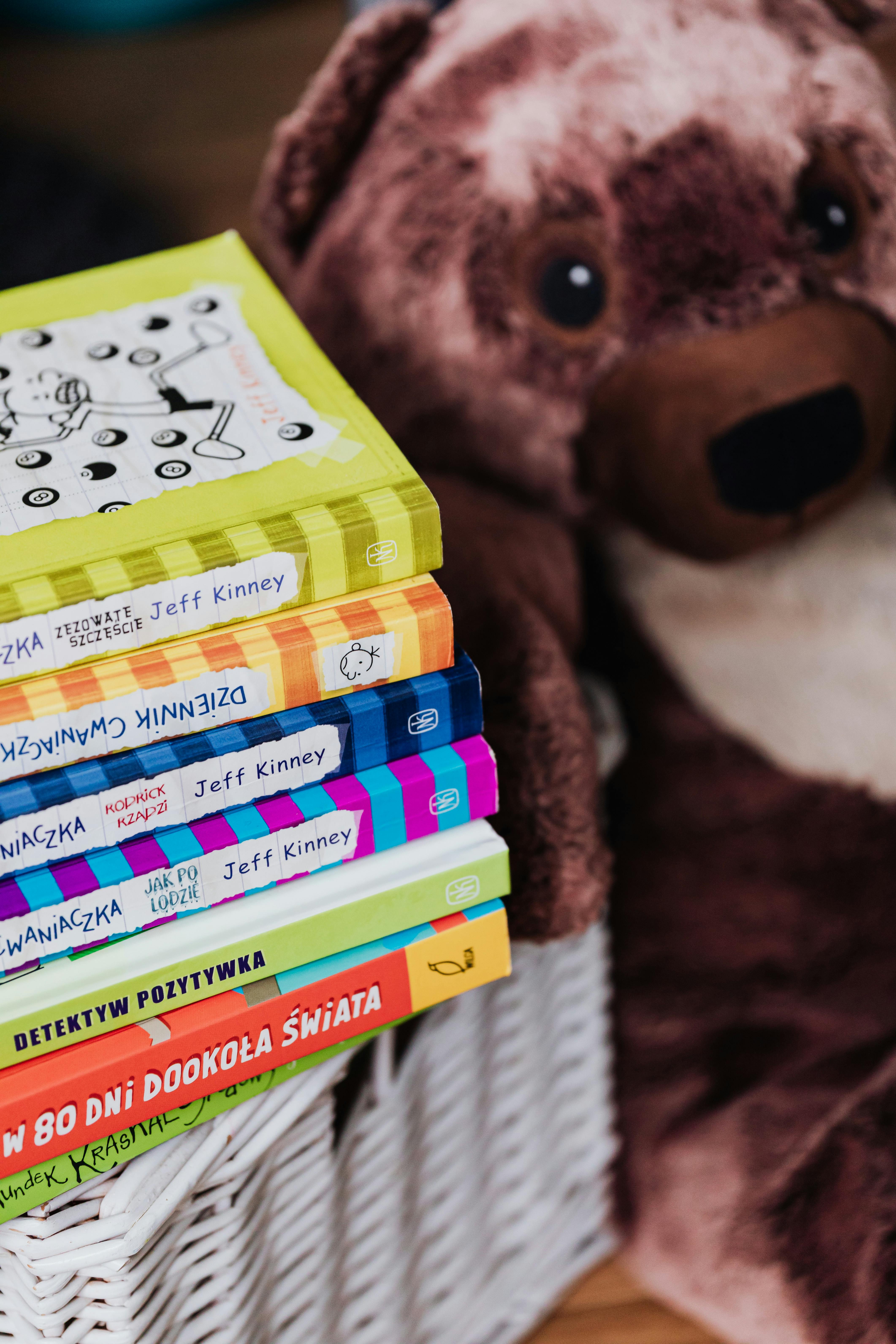 一堆色彩缤纷的儿童读物旁边，放着一只可爱的棕色泰迪熊