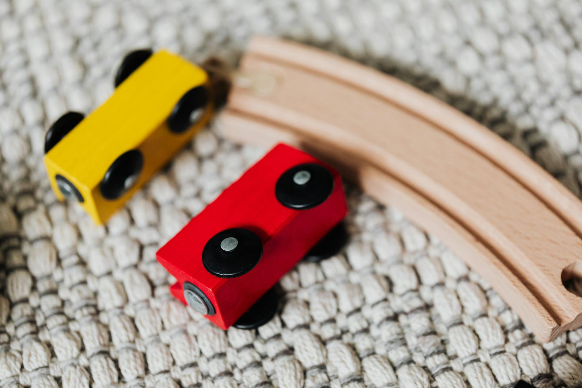 Close-up of red and yellow wooden toy cars on a textured carpet with a wooden track.