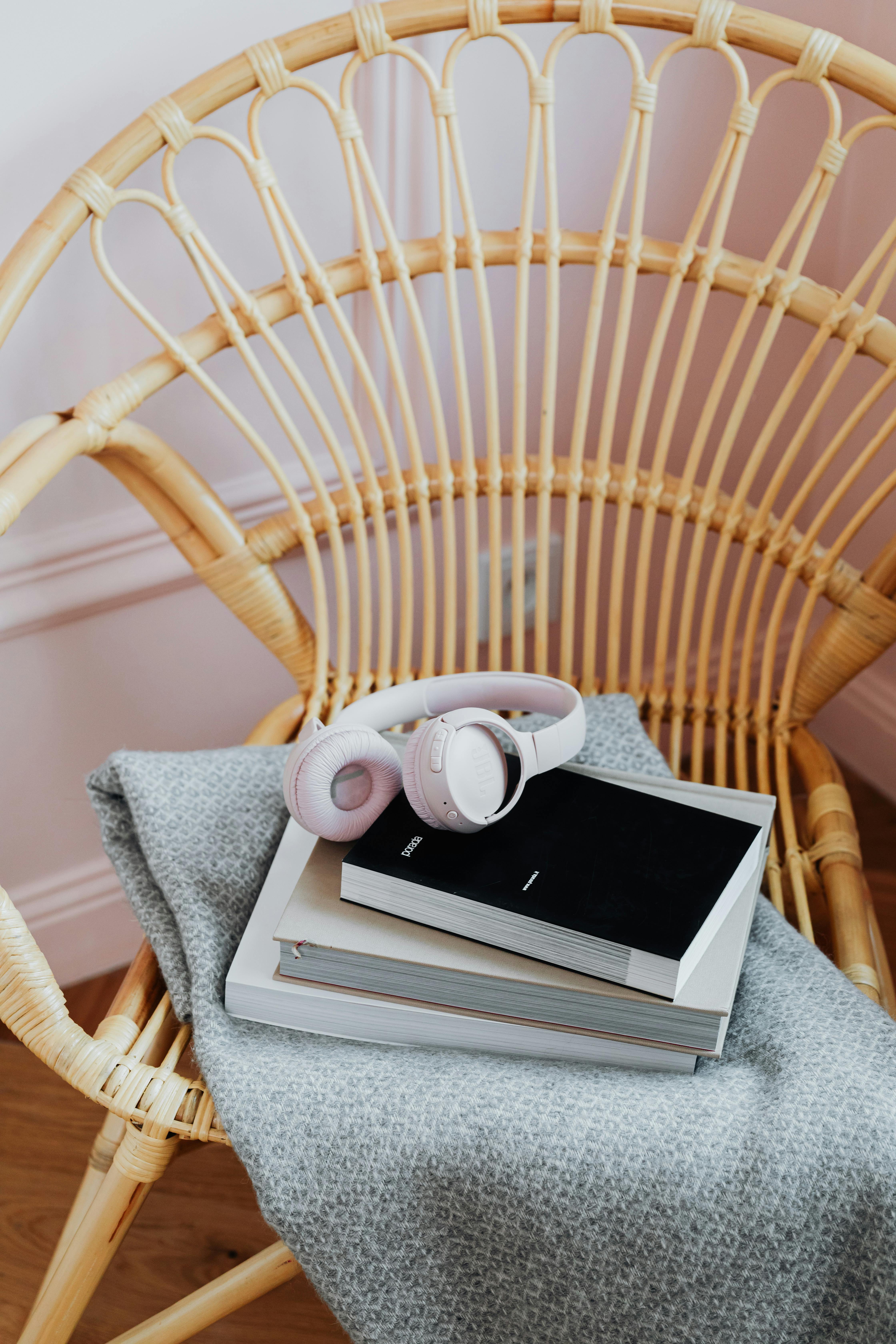 Free A rattan chair with books, a blanket, and wireless headphones creating a cozy reading nook. Stock Photo