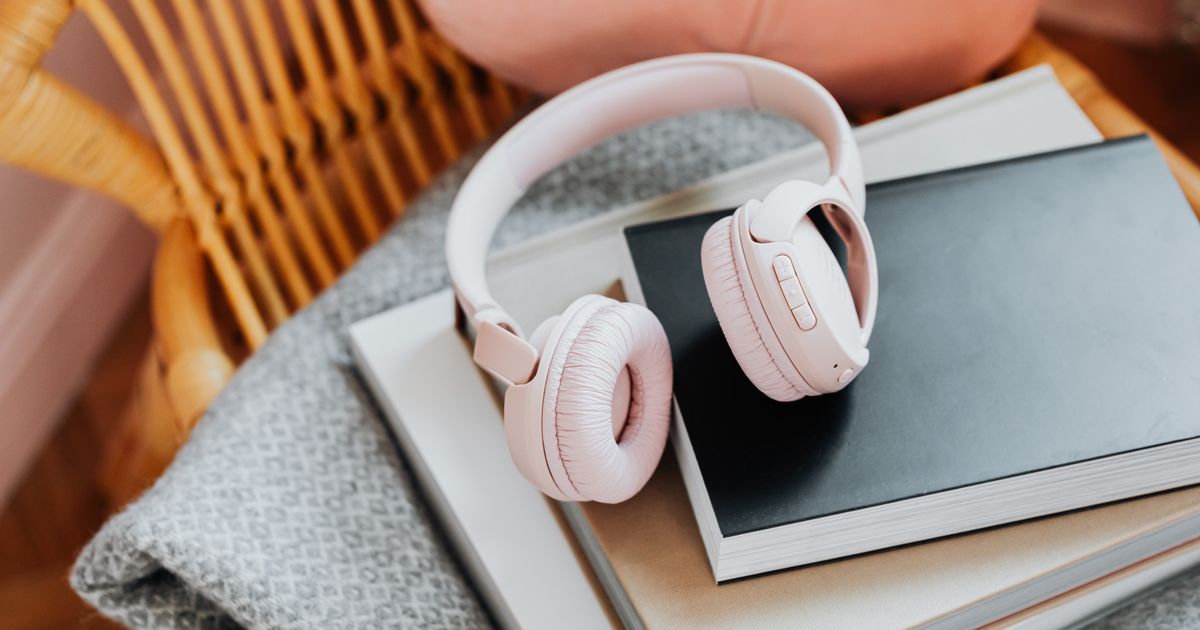 Pink wireless headphones resting on a stack of books on a rattan chair, enhancing a cozy vibe.