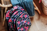 Vibrant floral patterned backpack on a wooden floor beside wooden furniture.