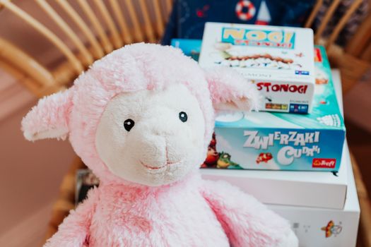 Close-up of a pink plush lamb alongside colorful board games, perfect for children's playrooms.