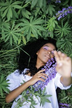 这幅户外肖像宁静祥和，描绘了一位躺在鹰嘴豆花与绿叶植物间的女子，捕捉到了夏日静谧的一刻