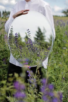一名男子手持圆镜，镜中映出郁郁葱葱的田野里盛开的韭菜花