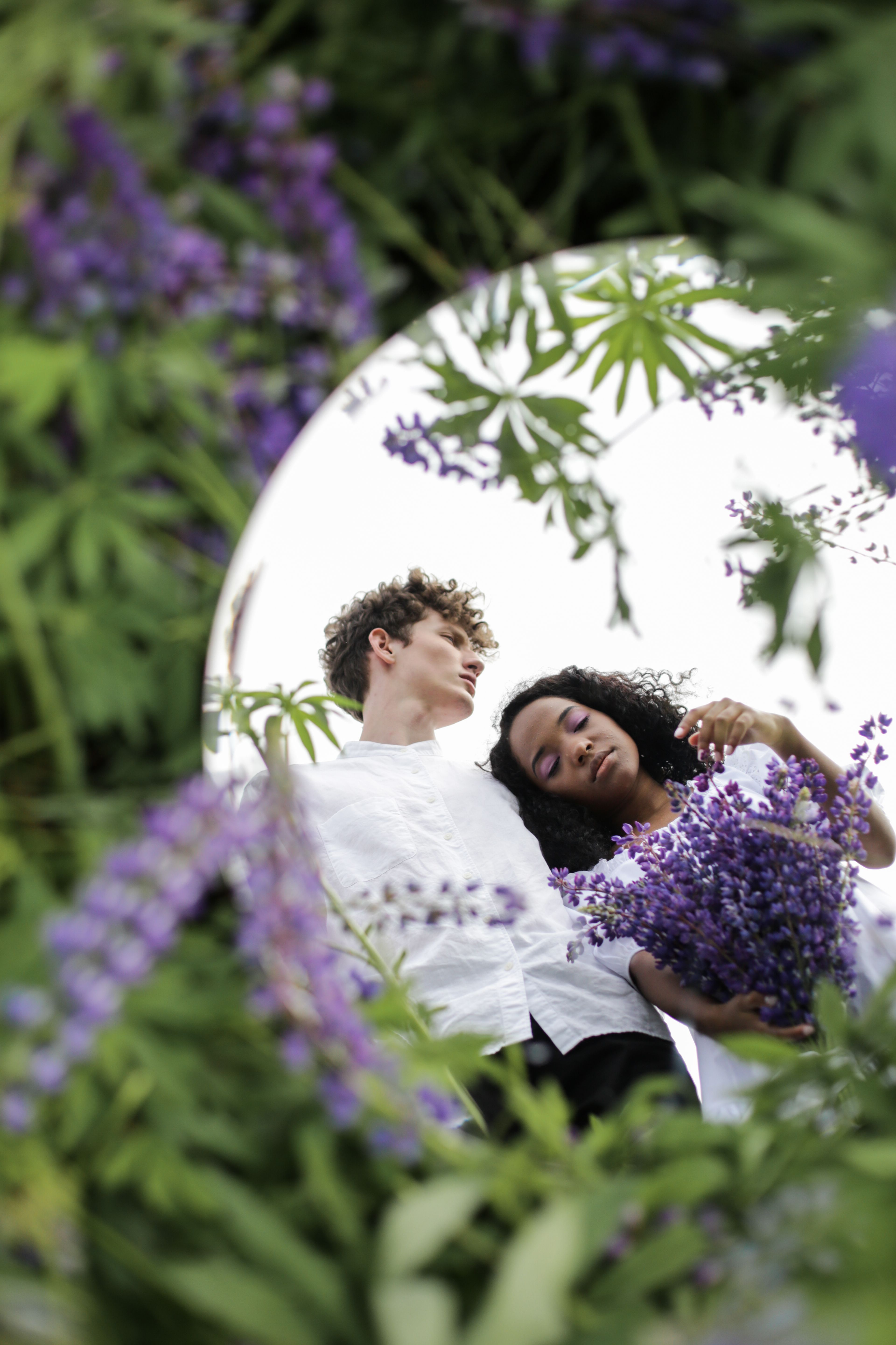 A diverse couple reflecting in a mirror surrounded by blooming lupins, symbolizing unity and nature.