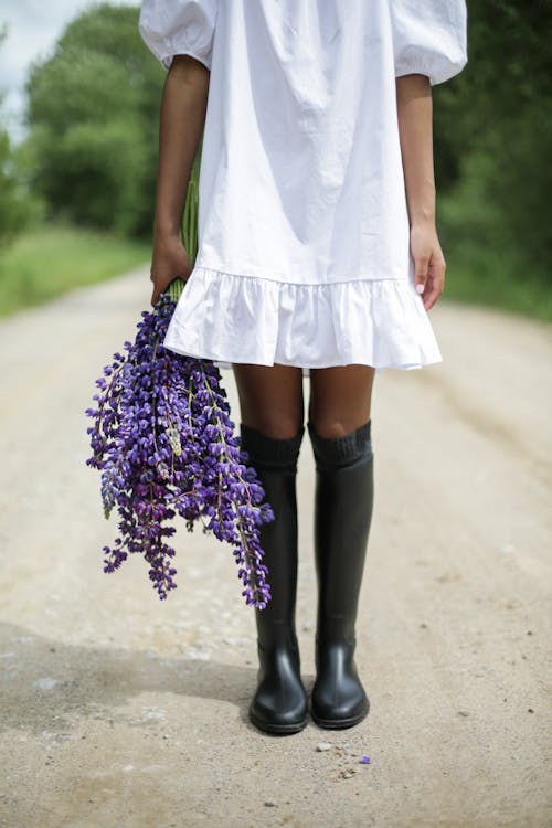 Woman in White Sleeveless Dress Holding Purple Flowers