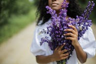 一名妇女在乡村小路上，手持鲜艳的紫色扁豆花