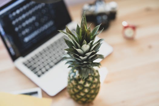 A fresh pineapple placed on a wooden desk next to an open laptop, creating a tropical workspace vibe.