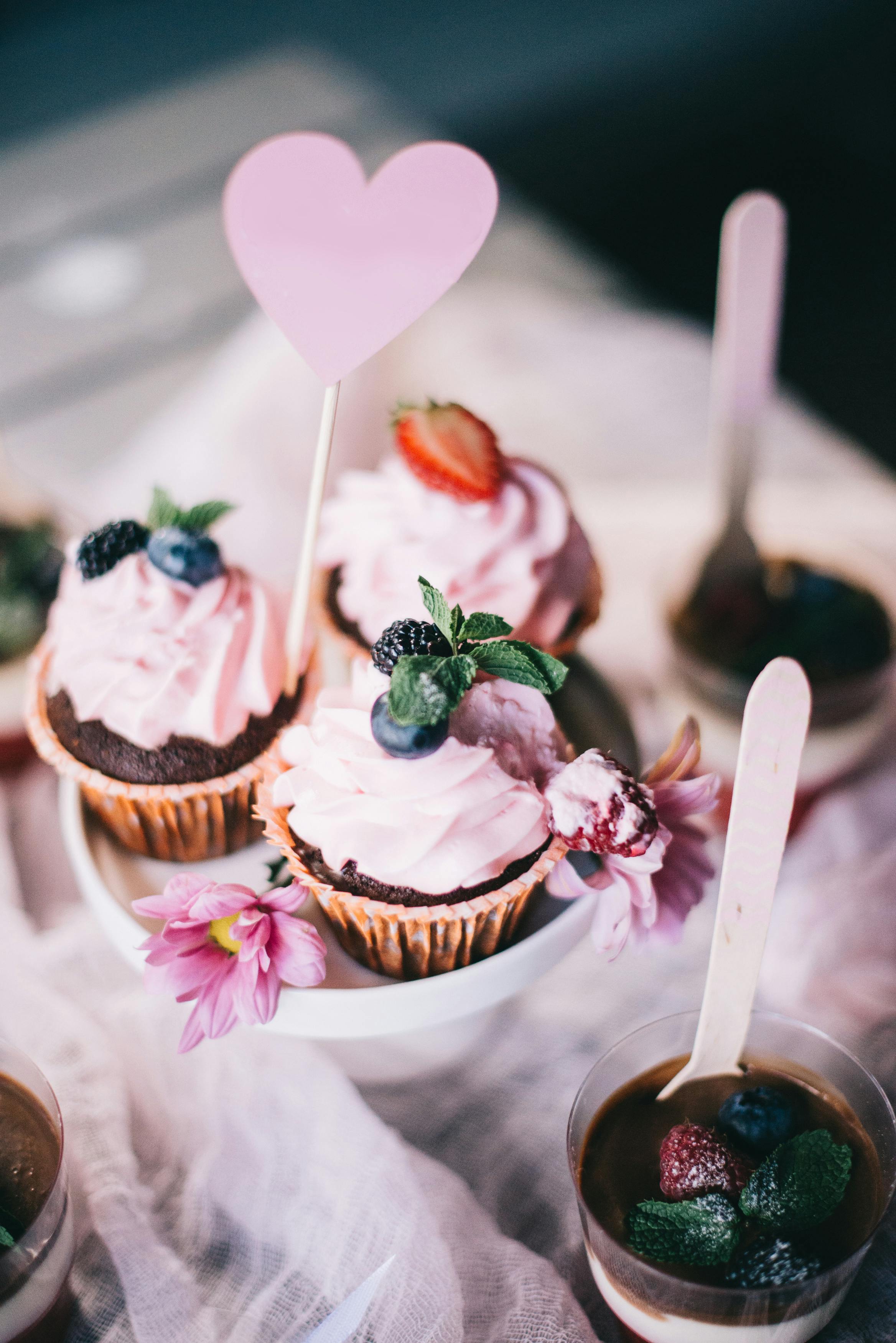 A beautiful arrangement of pink cupcakes topped with berries and mint on a dessert table.