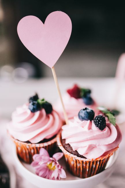 Delight in sweet pink cupcakes adorned with fresh berries and a heart topper, perfect for celebrations.