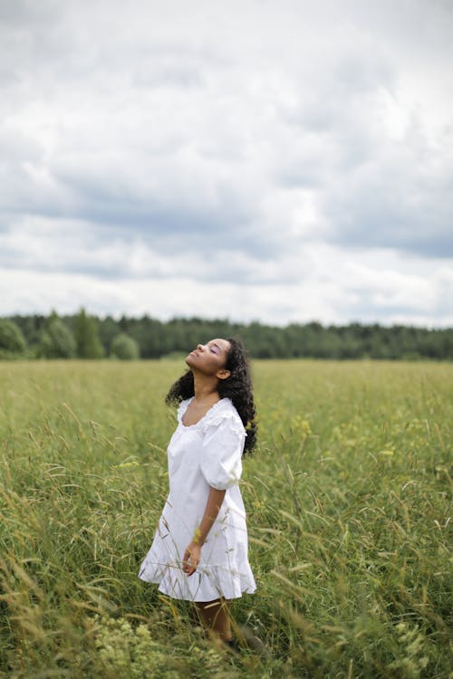 Woman in White Long Sleeve Dress Standing on Green Grass Field