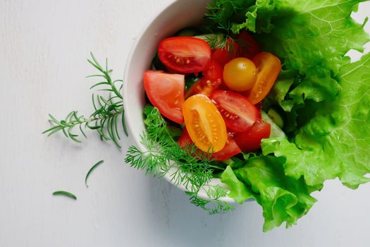 Top view of a fresh vegetable salad with tomatoes, lettuce, and herbs in a bowl.