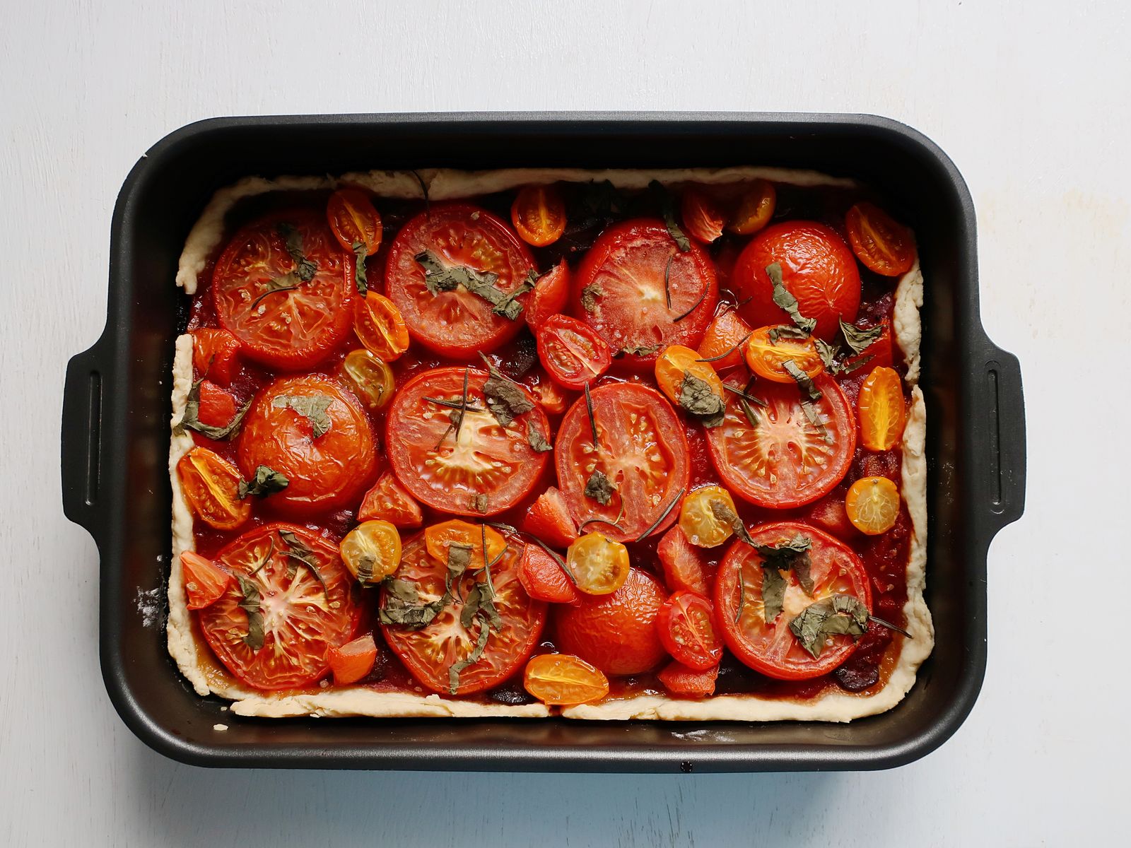 Baked tomato tart with fresh herbs in a dark rectangular baking pan