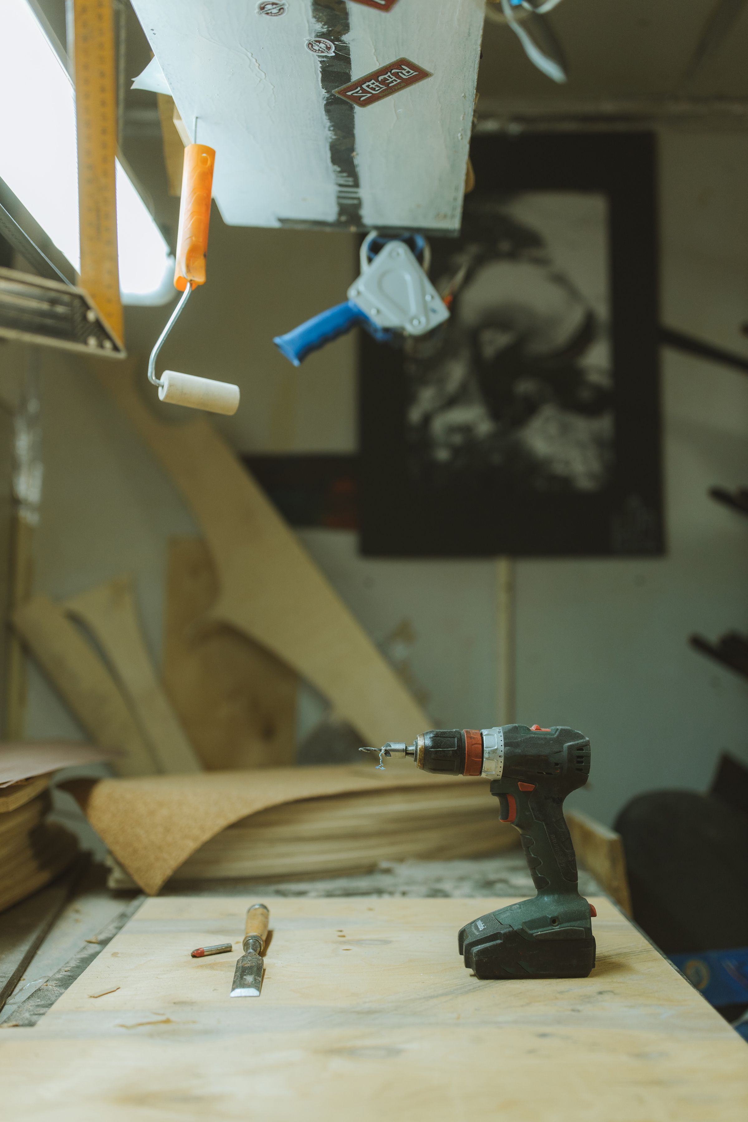Cordless drill, measuring tape, paint roller, screwdriver, and repair tools arranged on a wooden work surface
