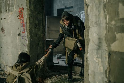 A man helps a woman in a desolate, post-apocalyptic urban environment.
