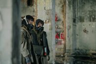 两个戴着防毒面具的人正在一座反乌托邦城市环境中探索废弃建筑