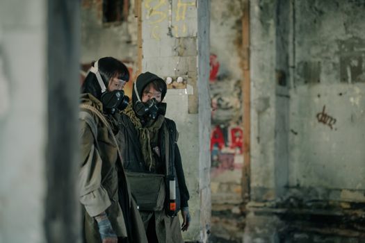 两个戴着防毒面具的人正在一座反乌托邦城市环境中探索废弃建筑