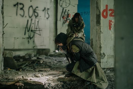 Two individuals exploring a decaying building with graffiti, embodying a post-apocalyptic theme.