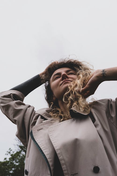 Positive woman touching hair under gray sky