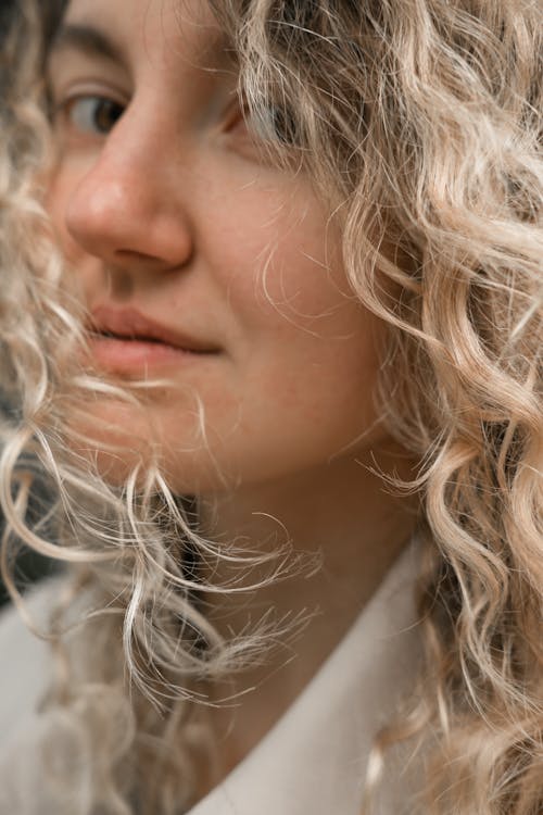 Beautiful young female in white clothing with curly blond  hair looking at camera with half smile