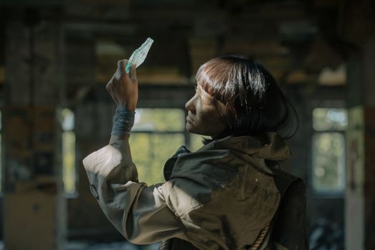 A woman examines glass in a sunlit, decaying urban environment.