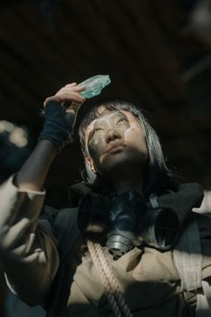 一个戴着防毒面具的女人在废弃的城市环境中拿着一块水晶