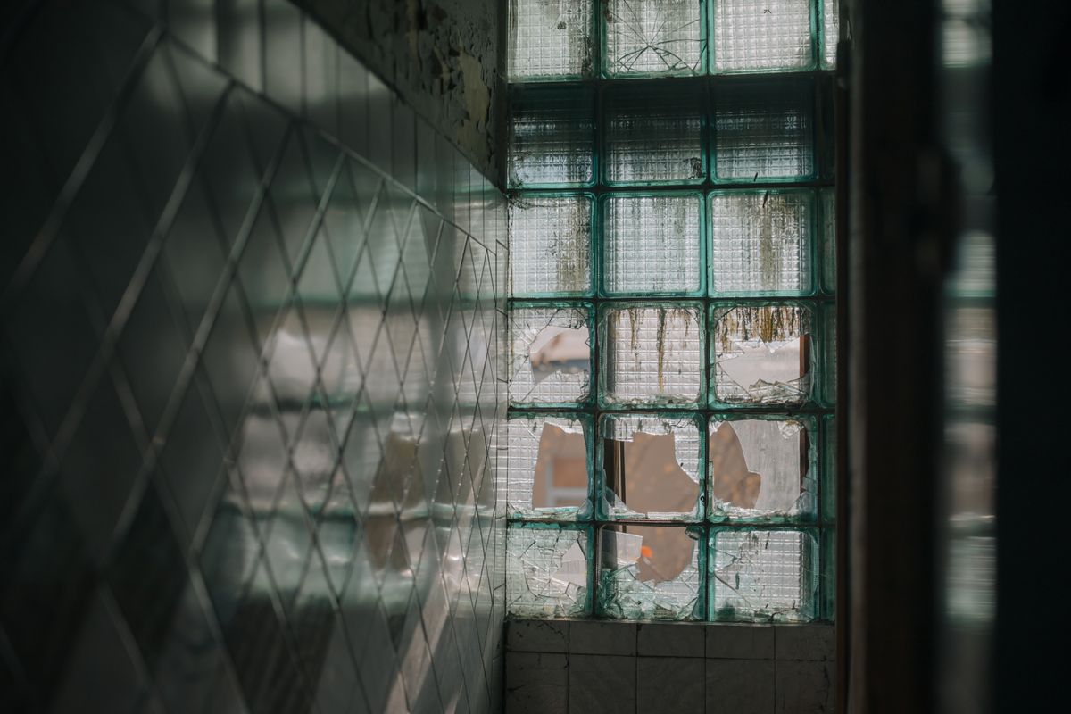 Dilapidated glass block window casting light in an abandoned urban building interior.