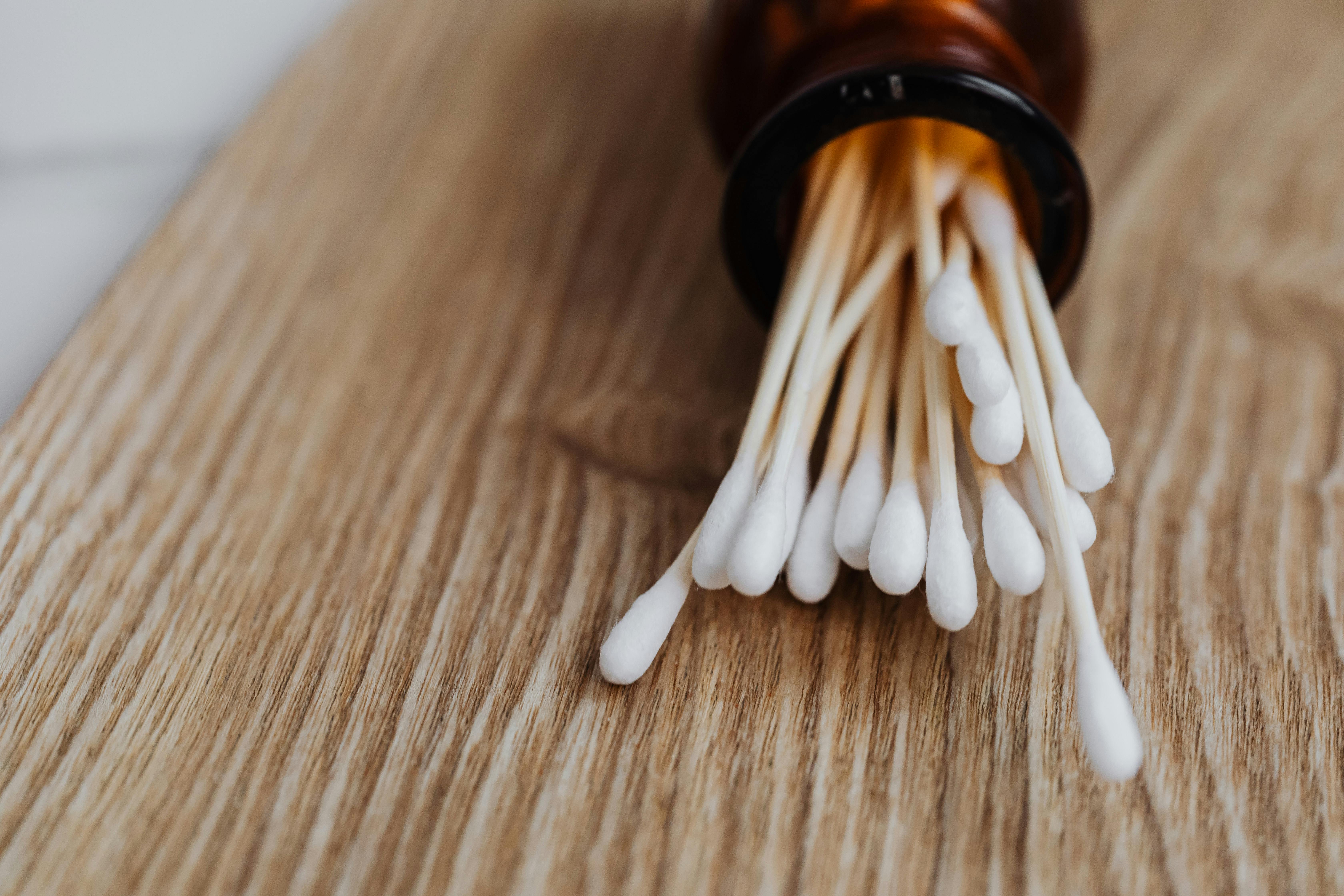 Close-up of cotton buds in a brown glass jar on a wooden table, emphasizing cleanliness and hygiene.
