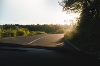 A winding road curves through a vibrant forest during a tranquil sunset, creating a serene and picturesque view.