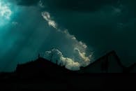 Dramatic scenery of overcast sky with heavy dark clouds floating over silhouettes of suburban cottages at night
