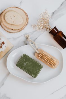 Flat lay of natural bath essentials, including soap, brush, and dried flowers on marble.