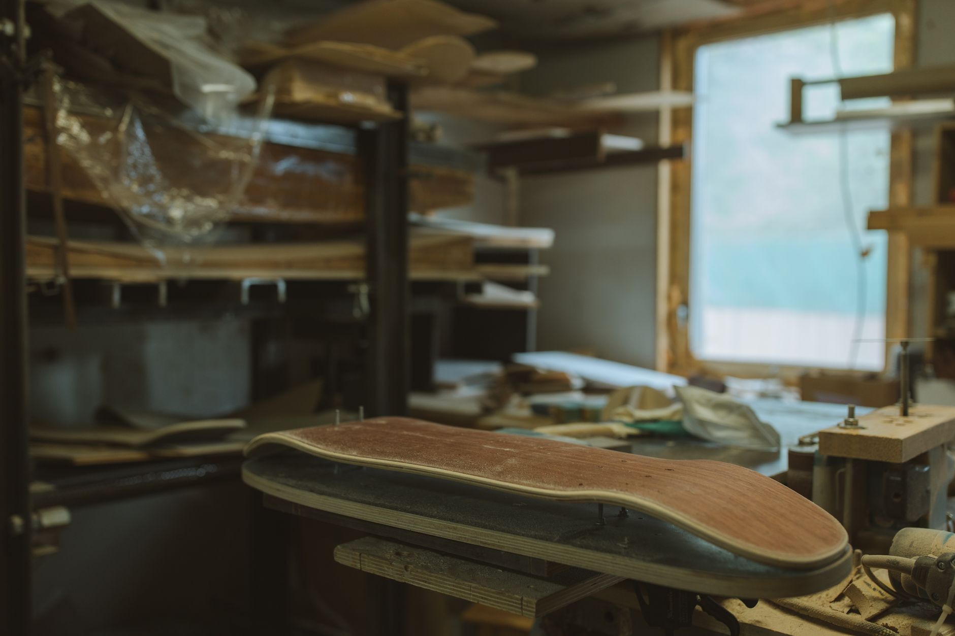 Close-up of skateboard deck grain, truck mounting holes, worn graphic, and measuring tape on workshop table