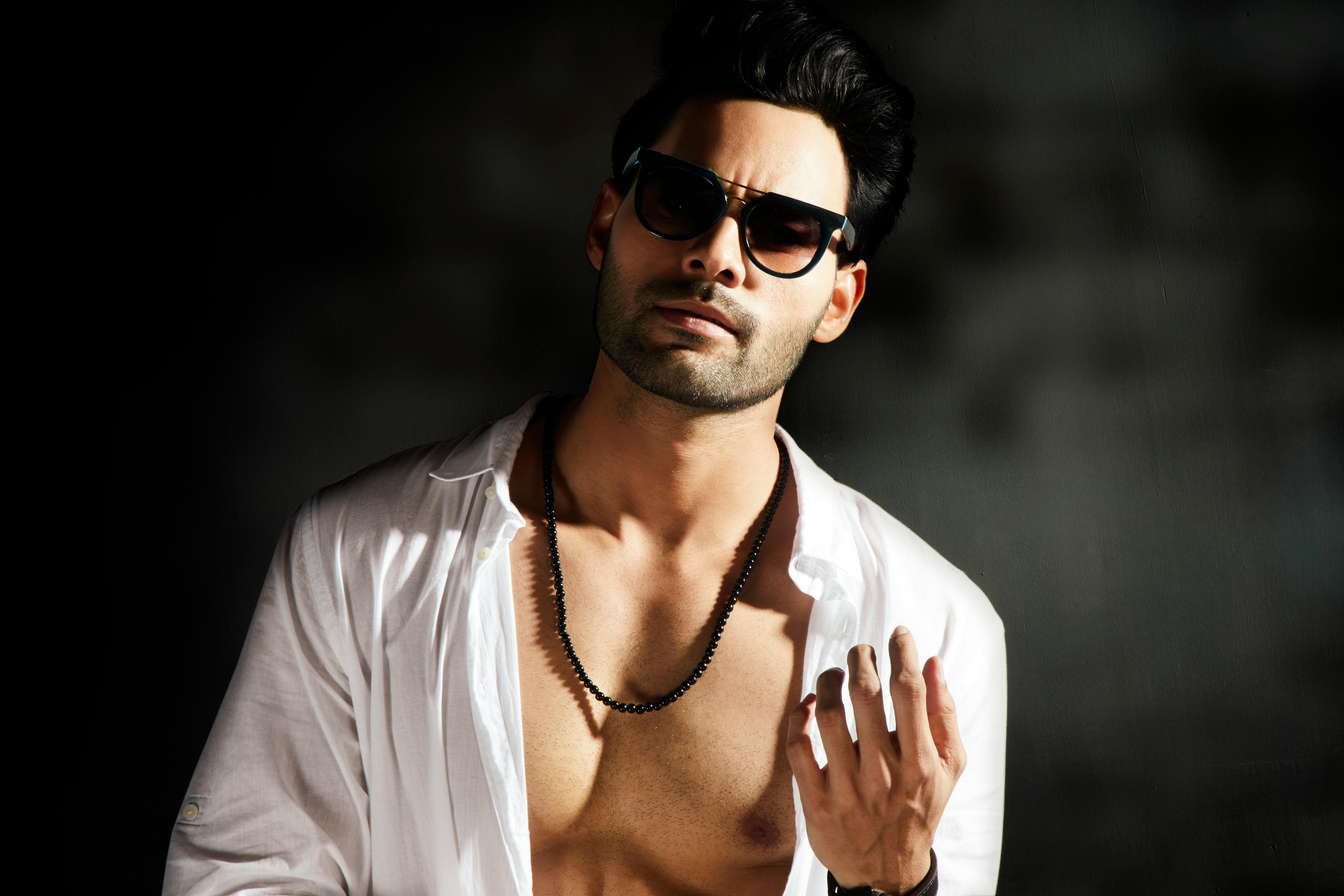 一位时尚男子戴着太阳镜，敞开衬衫，在戏剧性的灯光下自信地摆出姿势
