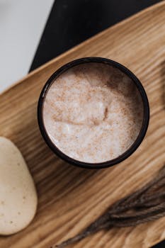Top view of a natural skincare cream surrounded by organic ingredients on a wooden tray, promoting eco-friendly beauty.