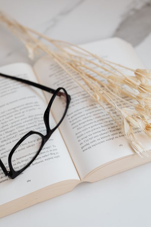 Free Open book with black glasses and dried flowers on a marble surface, creating a peaceful reading ambiance. Stock Photo