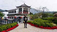 在香港昂屏村的人行道上，一名男子站在传统建筑和郁郁葱葱的花园旁