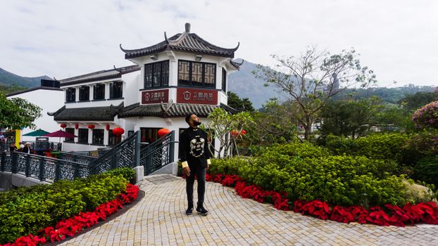 在香港昂屏村的人行道上，一名男子站在传统建筑和郁郁葱葱的花园旁