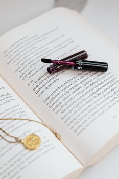 An open book featuring a lip gloss and a gold pendant necklace laid across its pages.