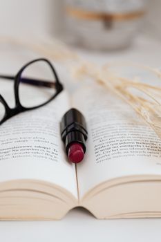 Elegant close-up of a lipstick and glasses on an open book, artistic composition.