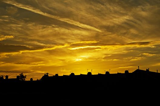 A stunning sunset casting golden hues over silhouetted city rooftops and clouds.