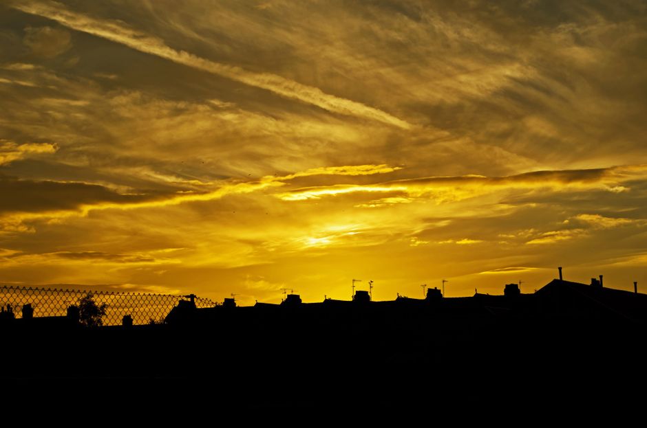 A stunning sunset casting golden hues over silhouetted city rooftops and clouds.