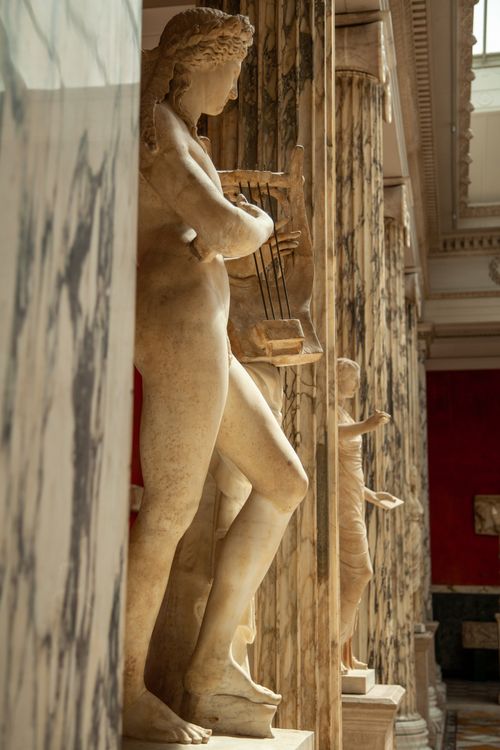 Free A marble statue of a Greek figure with a lyre in a museum gallery. Stock Photo