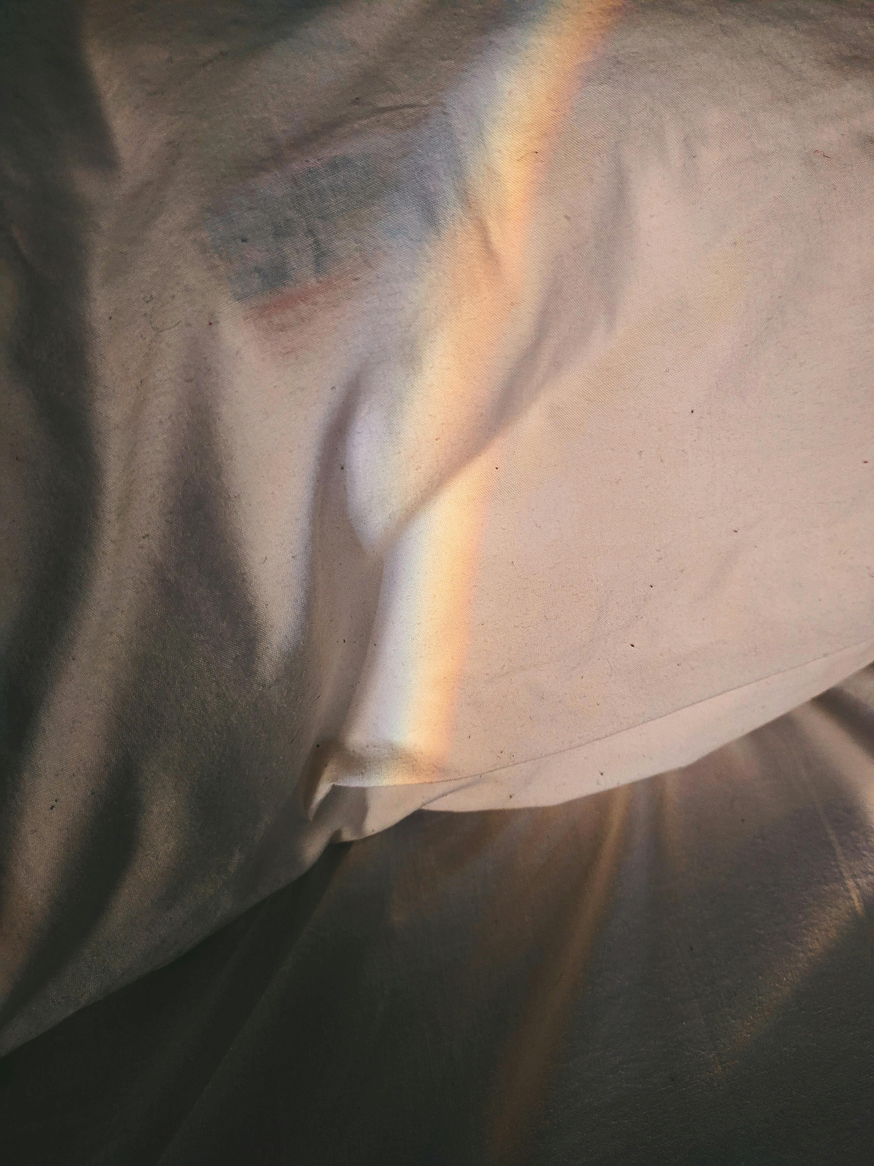 彩虹的微光映照在柔软亚麻布的褶皱上，营造出宁静梦幻的氛围