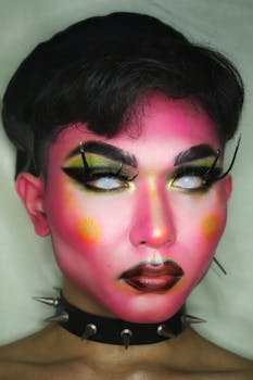 Man covered with bright pink paint and mysterious eye makeup in collar with spikes