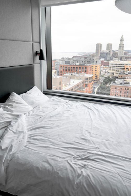 Free A modern hotel room with a view of downtown Boston, featuring a large window and comfortable bed. Stock Photo