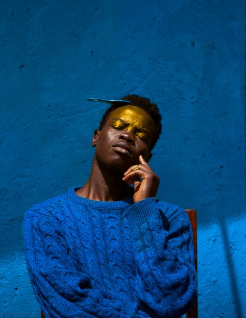 Dramatic portrait of a man against a rich blue background, exuding introspection and style.