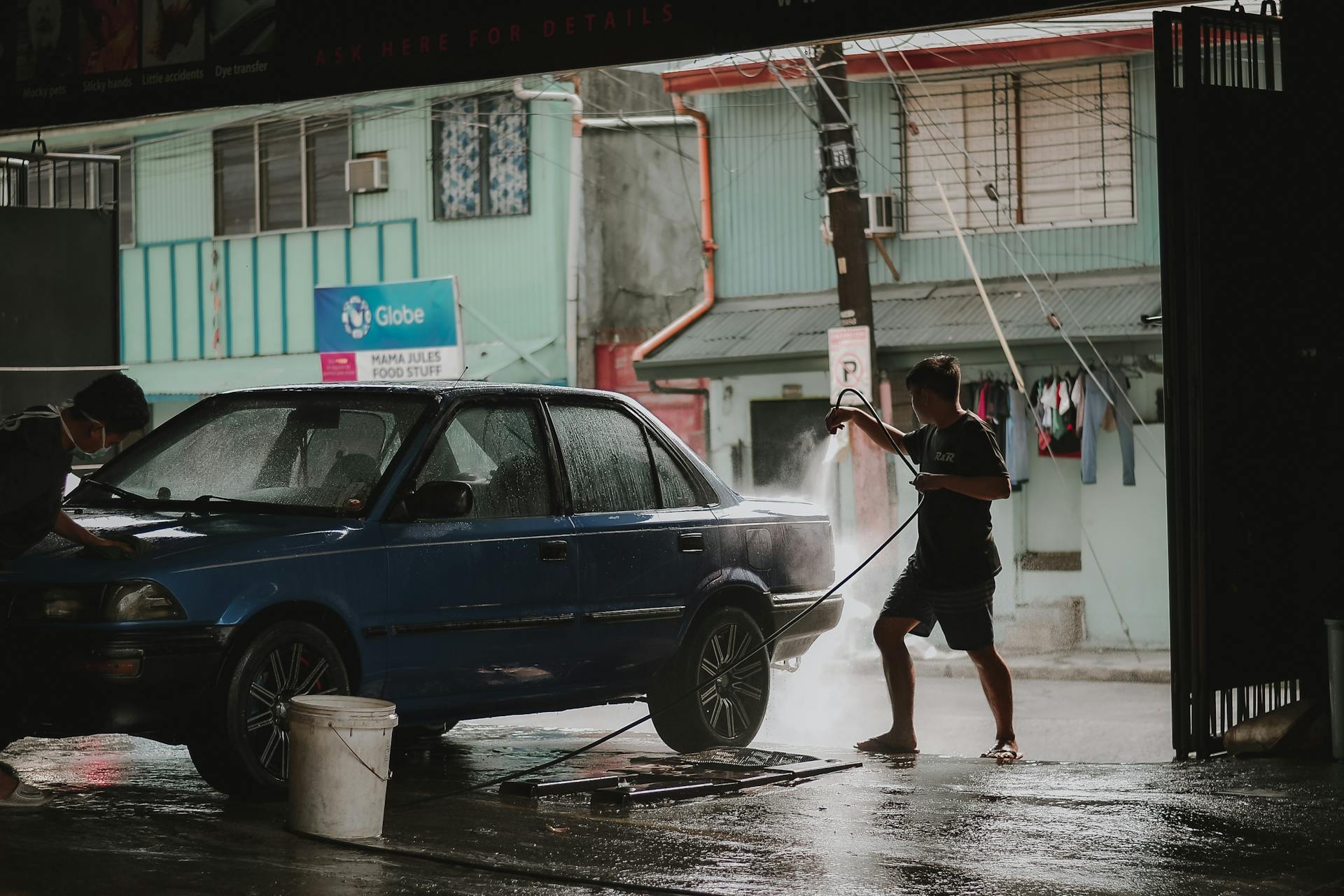 Photo of a Man Using a Hose to Wash a Car