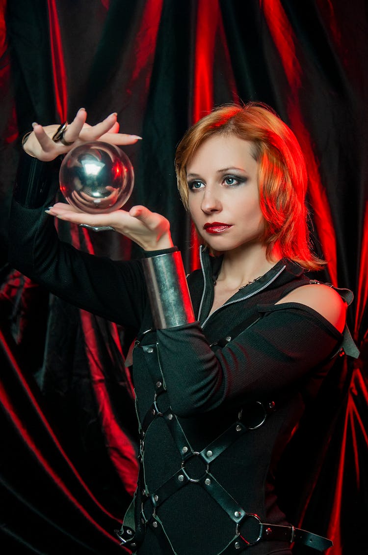 Female In Halloween Costume Looking At Shiny Ball In Red Light